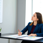 A professional woman, fully clothed in a modest business casual outfit, sitting at a clean, modern desk, actively engaged in drawing a colorful mind map on a large sheet of paper. Her expression is focused and thoughtful, indicating deep self-reflection. The background is a bright, organized office space with natural light. The scene conveys a sense of discovery and clarity. perfect anatomy, correct proportions, natural pose, well-formed hands, proper finger count, natural body proportions, safe for work, appropriate content, fully clothed, professional.